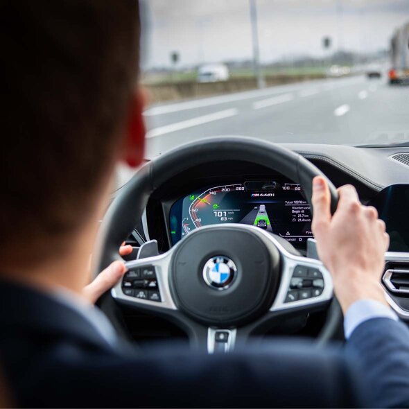 BMW-interieur-bestuurder-onderweg-handen-op-stuur-mobiel