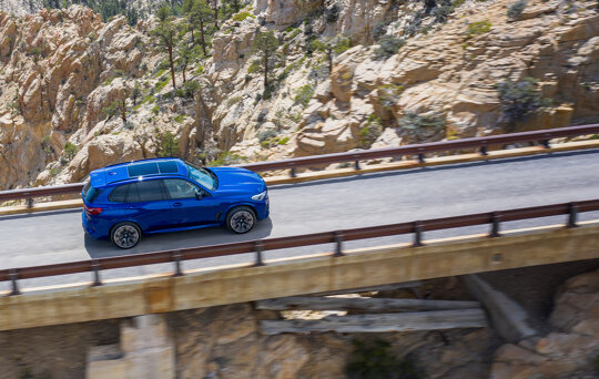 BMW_X5_M_Blauw_Exterieur_Rijdend_Brug_Zijkant_Bovenkant_Mobiel_Keram