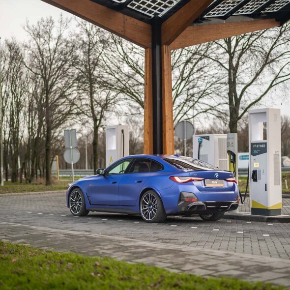 BMW-i4-matblauw-zijkant-achterkant-opladen-fastned-onderweg-mobiel